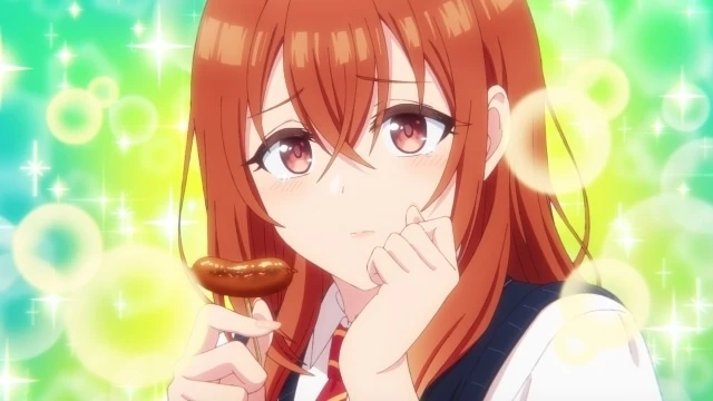 Primer plano de Ayaba Kohinata con expresión tímida y sonrojada, sosteniendo un aperitivo con brillo de fondo en una escena adorable del episodio 3 de Imōto no Tomodachi ga Ore ni Dake Uzai (La hermana de mi amiga solo me molesta a mí).