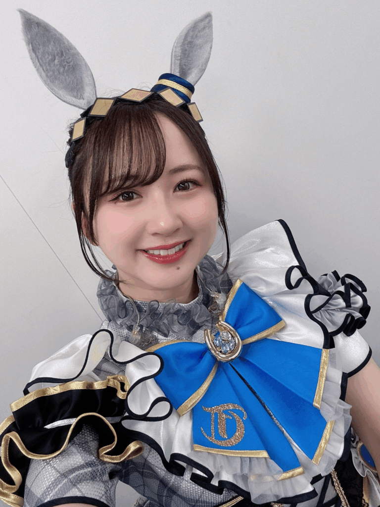 Intérprete caracterizada con un traje azul y blanco decorado con lazo dorado y orejas de caballo, inspirado en el personaje Oguri Cap de la serie Uma Musume: Pretty Derby.